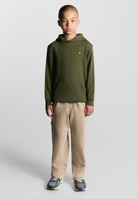 Felpa con cappuccio verde oliva con tasca frontale e logo, abbinata a pantaloni cargo beige e sneakers grigie con dettagli blu.