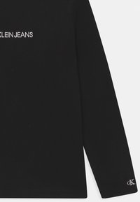 Czarna koszula z długim rękawem z białym haftem "CALVIN KLEIN JEANS" na klatce piersiowej oraz małym logo "CK" na mankiecie. Miękka, gładka tkanina.