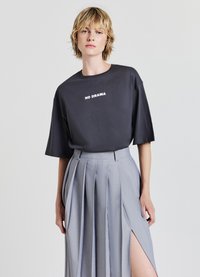 Maglietta grigia a maniche corte con il testo "NO DRAMA" in bianco, abbinata a una gonna plissee grigia chiaro con uno spacco laterale.