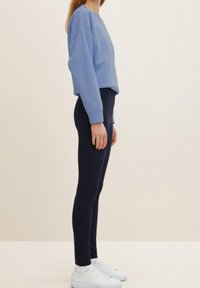 Felpa azzurra chiara con spalle scese, leggings navy e sneakers bianche con suole testurizzate. Tessuti lisci e design strutturato.