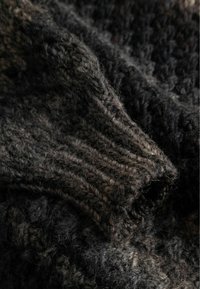 Textúrovaná pletenina v tmavosivých a čiernych odtieňoch, s hrubými, rebrovanými časťami a nadýchaným vzhľadom, ktoré zdôrazňuje jej teplo a jemnosť.