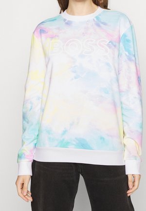 Osoba nosząca pastelową bluzę tie-dye z białym tekstem "BOSS" na klatce piersiowej i czarne spodnie, widoczna od ramion do bioder.