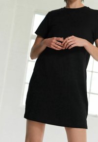 Robe t-shirt en coton noir avec manches courtes et coupe droite. Le tissu semble lisse et léger, avec des détails de couture subtils.