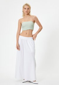 Jasnozielony bandeau top w prążki, zestawiony z zwiewną białą maxi spódnicą z elastycznym paskiem w talii. Gładka faktura, minimalistyczny design.