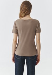 Top corto marrone a maniche corte con un ampio scollo arrotondato e una trama liscia, abbinato a jeans di denim scuro con delicate cuciture sui taschini posteriori.