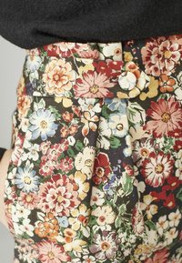 Pantalons en tissu imprimé floral avec un fond sombre, ornés de fleurs colorées de différentes formes, avec des plis à la taille et une fermeture à bouton.