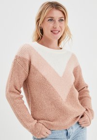 Maglione lavorato a maglia in un morbido rosa e bianco con una texture a costine. Presenta un motivo geometrico a zigzag, colletto rotondo e maniche lunghe.