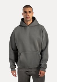 Grauer Kapuzenpullover mit lockerer Passform, ausgestattet mit einer Kängurutasche, gerippten Bündchen und einem kleinen Logo auf der Brust. Glatter, entspannter Stoff.