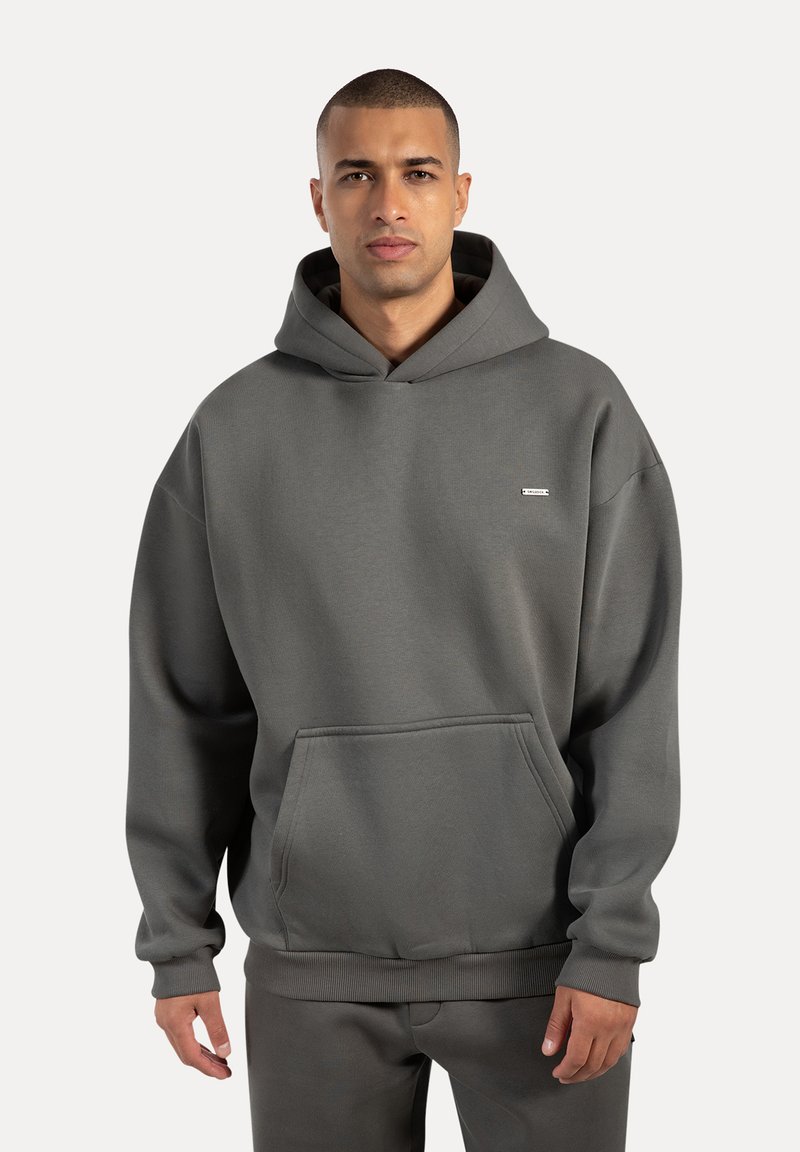 Grauer Kapuzenpullover mit lockerer Passform, ausgestattet mit einer Kängurutasche, gerippten Bündchen und einem kleinen Logo auf der Brust. Glatter, entspannter Stoff.
