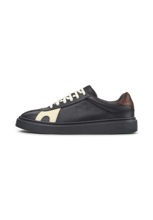 Schwarzer Ledersneaker mit weißen Schnürsenkeln, beigen Seitendetails, braunem Fersenriemen und dicker schwarzer Sohle mit Camper-Logo an der Seite.