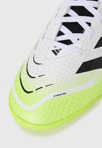 Hvit fotballsko med en teksturert, reptilaktig overflate, svarte detaljer og en livlig neongrønn såle. Har svarte lisser og logo-detaljer.