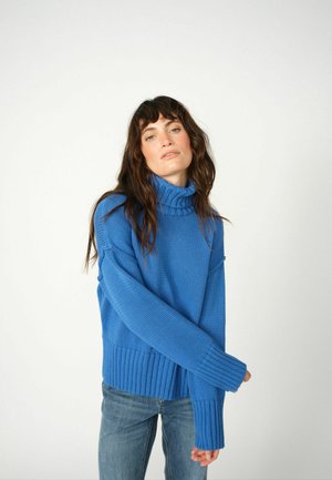 Blauer Strick-Turtleneck-Pullover mit strukturiertem Muster, mit gerippten Bündchen und Saum, kombiniert mit hellblauen Jeans.
