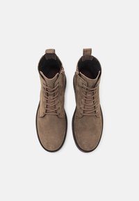 Brązowe zamszowe botki do kostki z sznurowaniem i zamkiem błyskawicznym z boku. Mają okrągły czubek i teksturowaną gumową podeszwę dla lepszej przyczepności.