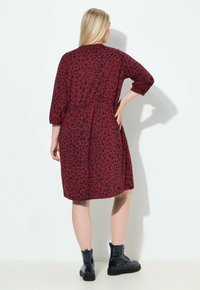 Punainen mekko mustalla leopardiprintillä, jossa on kolmanneksen hihat, gathered-vyötärö ja rento istuvuus, yhdistettynä mustiin nilkkasaappaisiin.