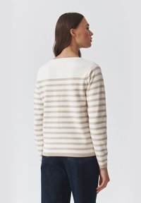 Sweter w paski w kolorze kremowym i jasnobeżowym, z okrągłym dekoltem, długimi rękawami i prążkowanymi mankietami. Miękka tekstura i luźny krój.