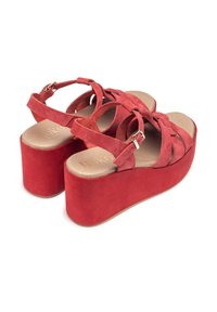Red suede platform sandals with crisscross straps and a large block heel. Features a soft inner sole and a metal buckle for adjustment.