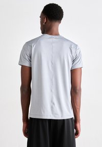 Tricou sportiv gri cu mânecă scurtă, având o textur�ă netedă și o cusătură dreaptă pe spate, asociat cu pantaloni scurți negri.