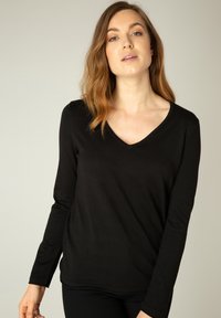 Zwarte langmouw V-hals top gemaakt van een rekbare ribstof met een relaxte pasvorm en een zachte textuur. De naaddetails zijn minimaal.