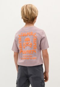T-shirt lilla a maniche corte con testo arancione audace e grafica di un teschio sulla schiena, realizzato in morbido cotone.