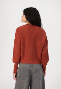 Rustfarget strikkegenser med avslappet passform, teksturert ribbing og drop shoulders, kombinert med høy midje grå vide bukser.