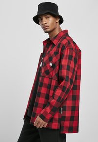 Rød- og sortternet flannel skjorte, knaplukning med en enkelt brystlomme, lange ærmer og et side-tag. Båret over en sort skjorte.