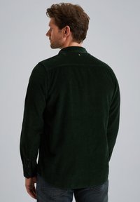 Donkergroene corduroy blouse met een kraag met knopen, lange mouwen en een gestructureerde afwerking. Kenmerkt een subtiele achterste yoke-detail en knoopmanchetten.