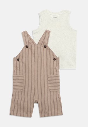 Λευκό αμάνικο μπλουζάκι για toddlers σε συνδυασμό με μπεζ ριγέ κοντά σαλοπέτες με μπροστινές τσέπες και κουμπιά στα τιράντες και στα πλαϊνά.