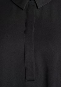 Detailní záběr na černou košili s límečkem, zakrytým knoflíkovým zapínáním a jemnou tkaninou.