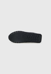 Black rubber shoe sole with thick, textured tread and pronounced "HUGO" branding. Features a raised, ridged design for traction.
