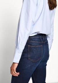 Chemise à manches longues bleu clair avec poignets à boutons, associée à un jean denim bleu foncé avec poches arrière et coutures contrastantes.