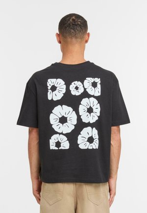 Camiseta de algodón negra de corte holgado con patrones florales blancos impresos en la parte trasera en varios tamaños. Cuello redondo, mangas cortas.