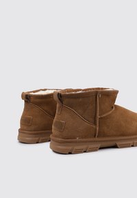 Braune Wildleder-Stiefeletten mit weichem Futter aus Fell, Gummisohle und gesticktem Design. Verfügt über ein Schlaufenetikett auf der Rückseite für einfaches Anziehen.