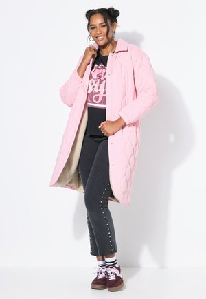 Pink quilted long coat with snap buttons, beige lining, paired with black jeans featuring studded accents and burgundy sneakers.