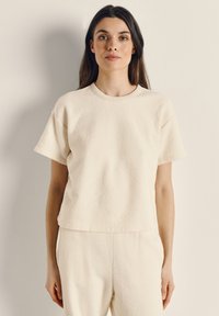 Lysebeige kortærmet top i tekstureret stof med rund halsudskæring. Den har en afslappet pasform og er kombineret med matchende bukser.