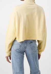 Rajattu vaaleankeltainen neulepaita, jossa korkea kaulus ja pitkät hihat. Pehmeä materiaali, väljä malli, yhdistetty vaaleansinisiin farkkuihin, joissa takataskut.