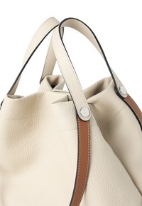 Strukturierte Lederhandtasche in Creme mit hellbraunen Akzenten und schwarzem Besatz. Verfügt über zwei Henkel und einen Kordelzugverschluss.