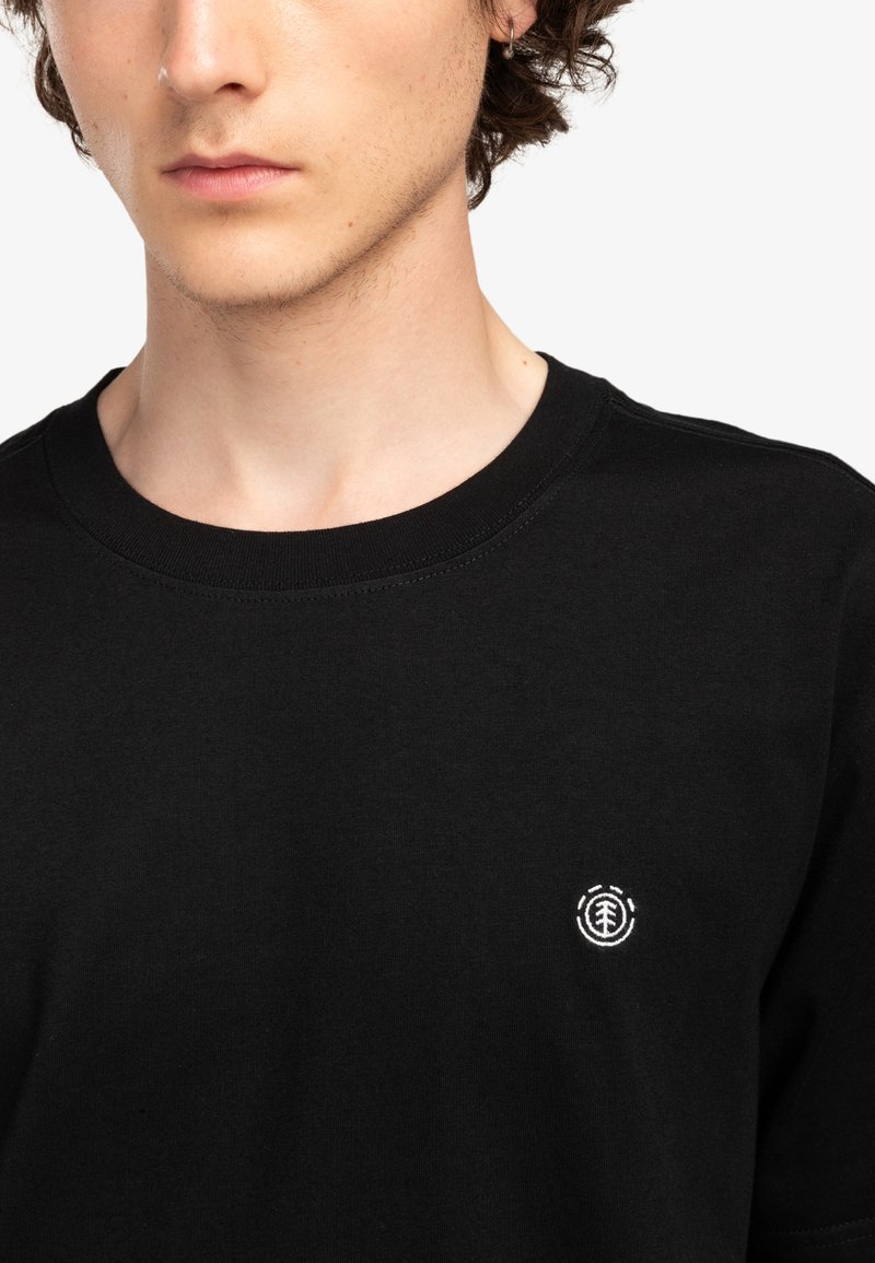 Czarna bawełniana koszulka z okrągłym dekoltem i krótkimi rękawami. Posiada małe białe logo haftowane na lewej piersi. Gładka faktura.