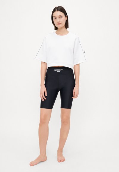 Vit kortärmad tröja i jersey, matchad med höga svarta shorts med en märkeslogotyp på midjan. Slät, åtsittande textur.