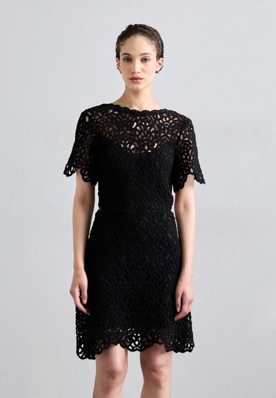 Vestido de encaje negro con intrincados patrones florales, mangas cortas y un dobladillo en formas onduladas. Silueta ajustada que acentúa la cintura.