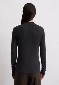 Schwarzes, geripptes Langarmoberteil mit Kragen. Verfügt über ein tailliertes Design und strukturierter Stoff. Die Rückansicht zeigt die Länge und Details der Ärmel.