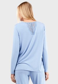 Top long à manches longues bleu clair avec des détails en dentelle au niveau de l'encolure arrière, fabriqué dans un tissu doux avec une coupe décontractée.