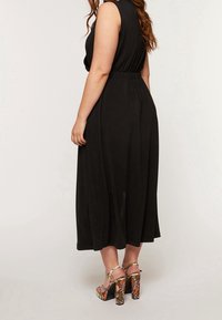 Svart ärmlös klänning med en figursydd midja och en flödande kjol. Matchas med högklackade sandaler med ett ormskinsmönster i livliga färger.