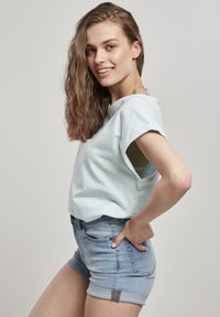 Világoskék, rövid ujjú, puha anyagból készült felső, amelyet fakult, farmer rövidnadrággal párosítanak, amelynek hajtott szárú fazonja és bronz részletei találhatóak a zsebeknél.