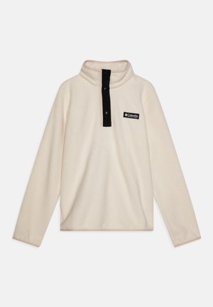 Pulóver de felpa color crema con cuello alto, con tapeta de botones negra y un pequeño parche con logo negro en el lado izquierdo. Textura suave, mangas largas.