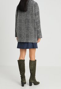 Grå mönstrad kappa med loose fit, bärs över en marinblå kjol och kombineras med knähöga stövlar i olivgrön mocka.