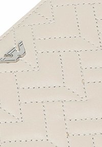 Beige kůže s tkaným vzorem, zdobená stříbrnými detaily. Textura je hladká, zvýrazněná kontrastním prošitím.