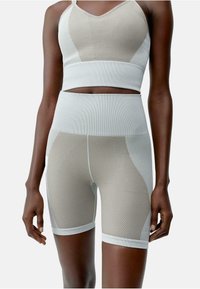 Tweedelig sportset in lichtbeige en wit. De top heeft een geribbelde textuur met een V-hals, terwijl de shorts horizontale strepen en een hoge tailleband hebben.