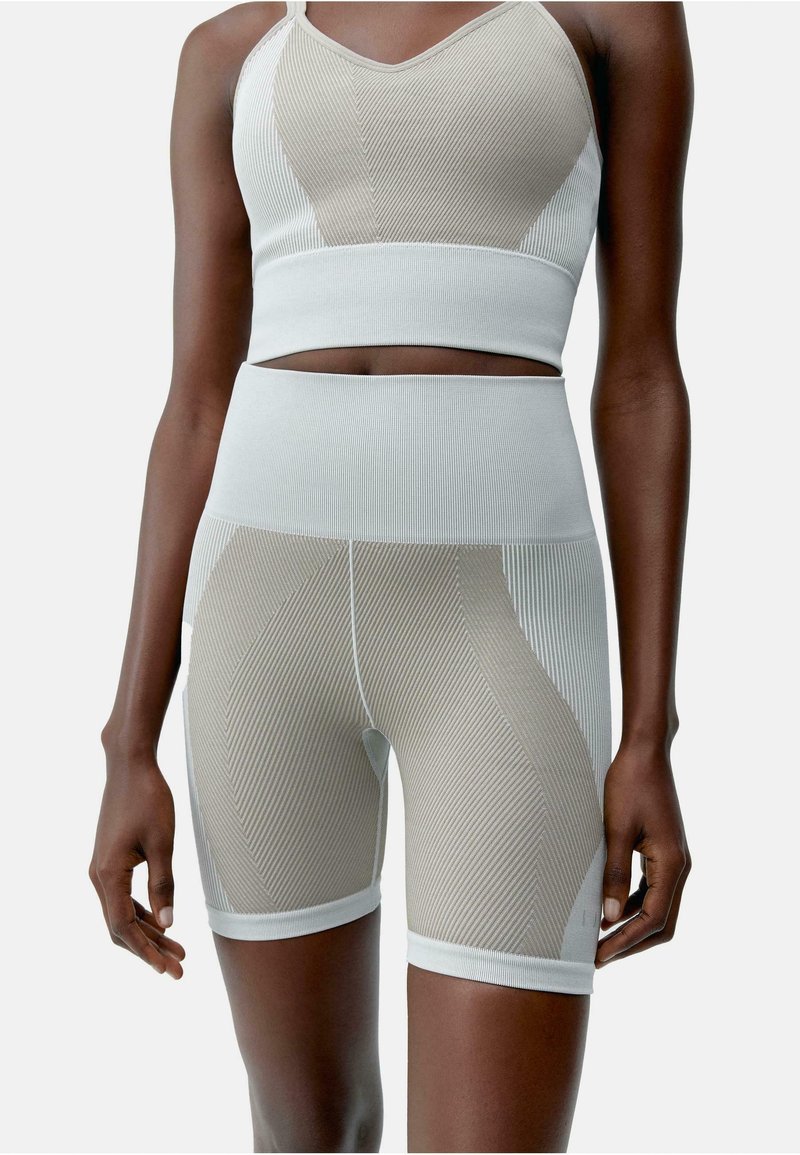 Tweedelig sportset in lichtbeige en wit. De top heeft een geribbelde textuur met een V-hals, terwijl de shorts horizontale strepen en een hoge tailleband hebben.
