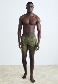 Shorts de bain vert olive avec une taille élastique et un cordon de serrage, présentant une texture lisse et une coupe décontractée.