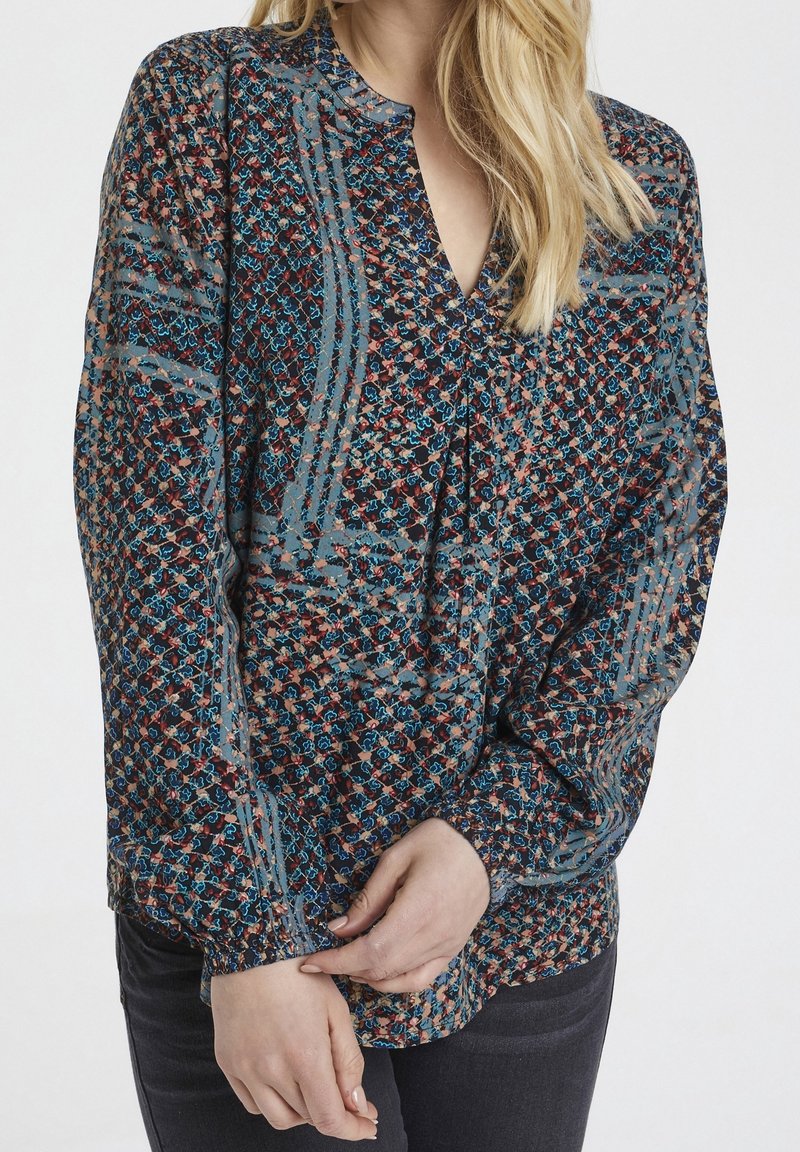 Bluzka z długim rękawem z przezroczystego materiału, ozdobiona kwiatowym wzorem w kolorze niebieskim, czerwonym i beżowym, z dekoltem w serek i marszczonymi mankietami.